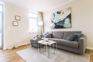 Ein modernes Wohnzimmer mit einem grauen Sofa, einem weißen Couchtisch und einem großen abstrakten Gemälde an der Wand.