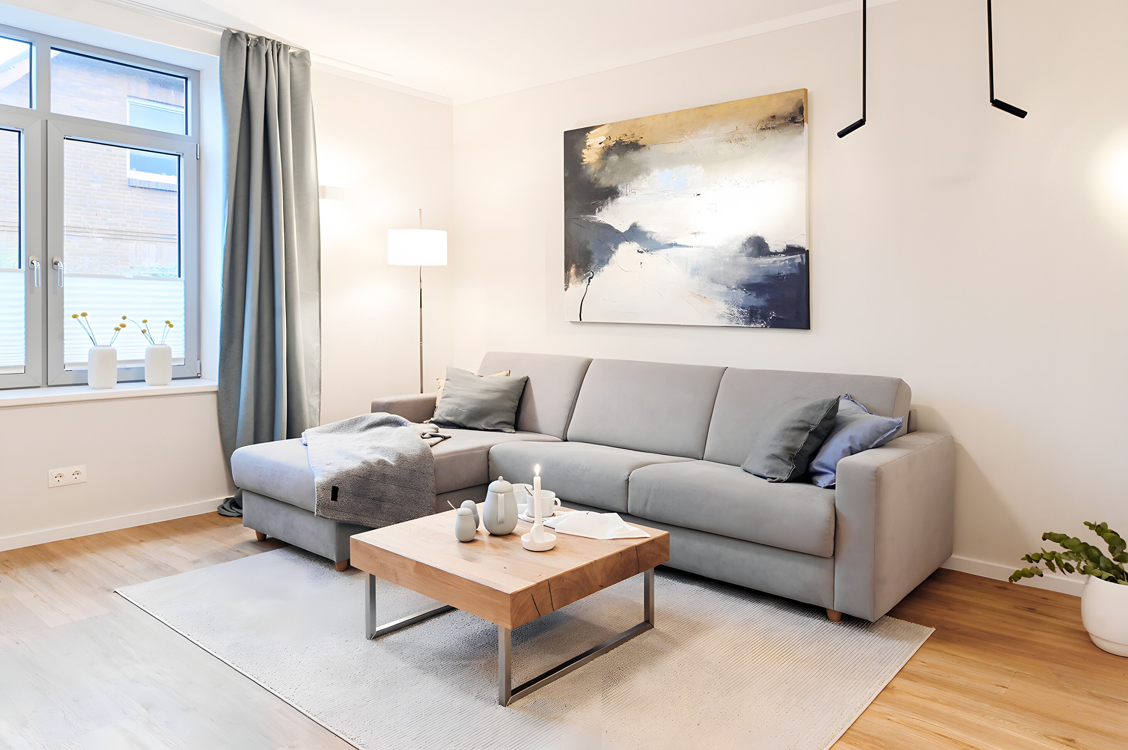 Een moderne woonkamer met een grijze bank, een houten salontafel en een schilderij aan de muur.
