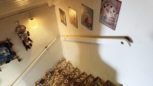 Un escalier avec une rampe blanche, un attrape-rêves et des œuvres d’art murales, notamment une affiche représentant une femme et une autre représentant une femme dans une cuisine.