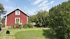Une grange rouge avec une porte et une fenêtre blanches, entourée d’herbe verte et d’arbres.