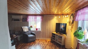 Un salon chaleureux avec un plafond en bois, un fauteuil confortable, un téléviseur à écran plat et une fenêtre avec des rideaux.