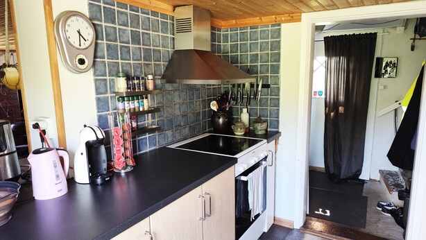 Une cuisine dotée d’un plan de travail noir, de meubles en bois, d’une hotte en acier inoxydable et d’un dosseret carrelé.