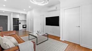 Een moderne woonkamer met een leren bank, een glazen salontafel en een flatscreen televisie die aan de muur is bevestigd.