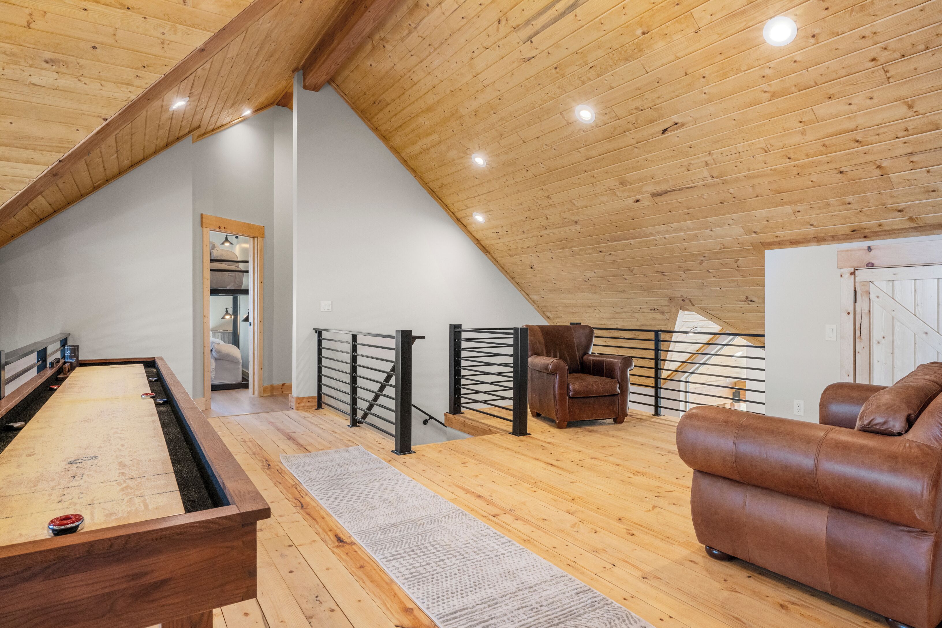 A spacious loft with a wooden ceiling, a pool table, a leather sofa, and a staircase.