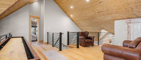 A spacious loft with a wooden ceiling, a pool table, a leather sofa, and a staircase.