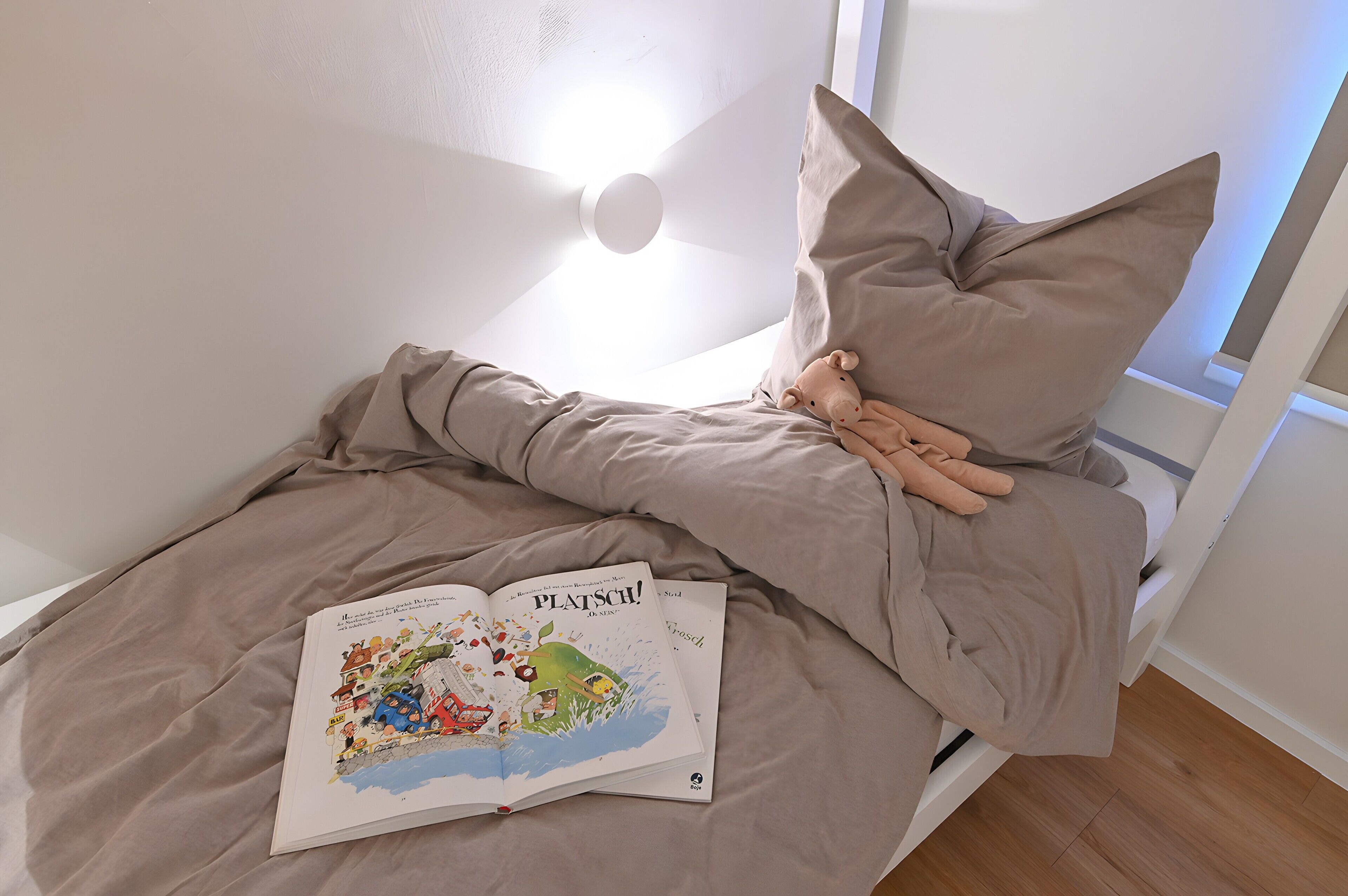 A bed with a book titled 'PLATSO!' and a stuffed toy.