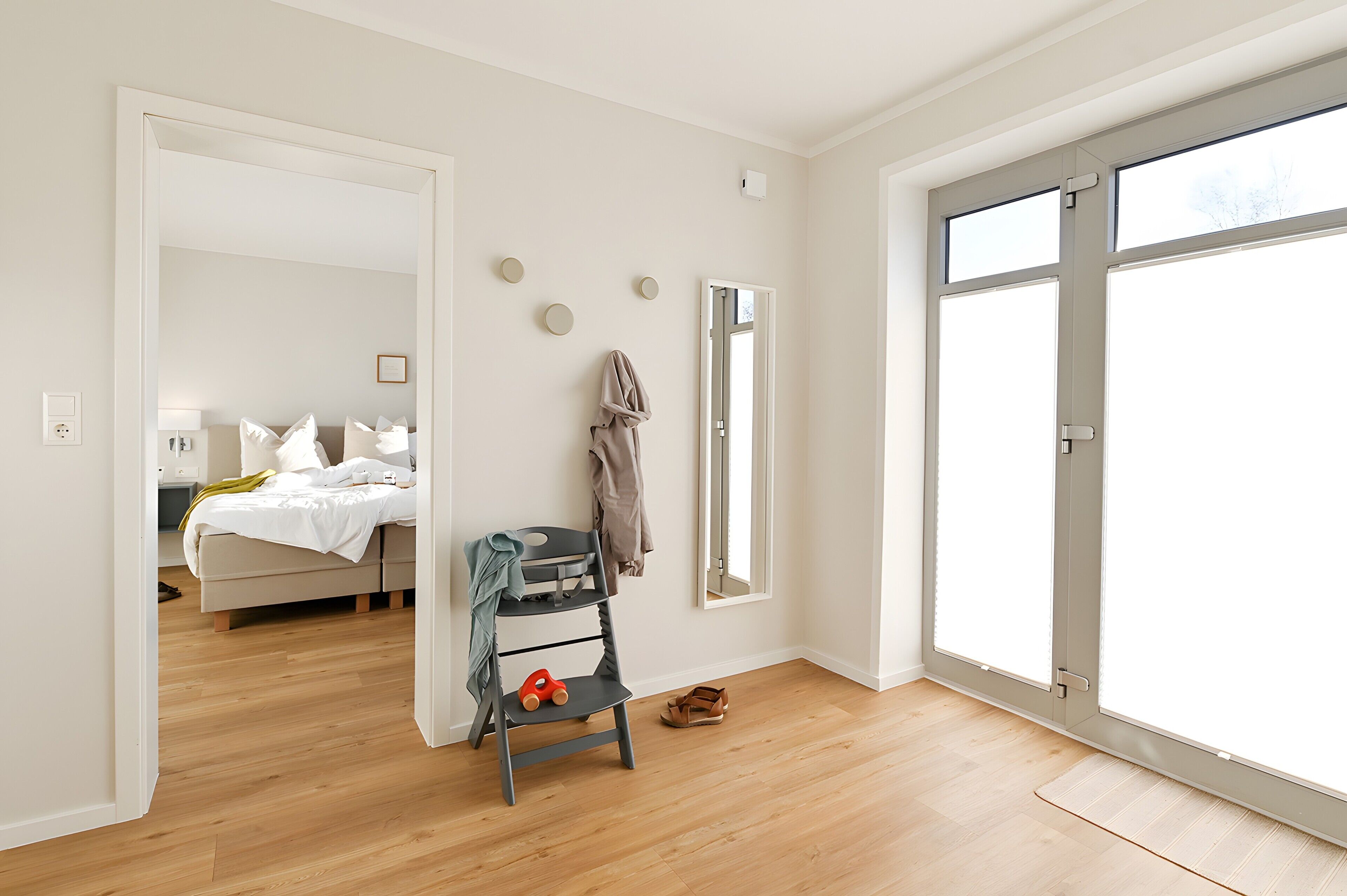 Ein modernes Schlafzimmer mit einem Bett, einem Sessel, einem kleinen Tisch und einem großen Fenster.