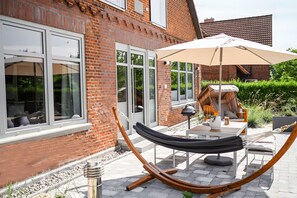 A brick house with a patio, a hammock, outdoor furniture, and a large umbrella.