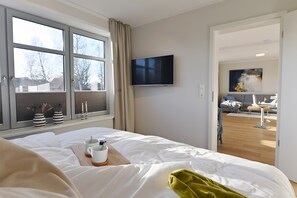 A hotel room with a bed, a TV, a window with curtains, and a view of the living area.