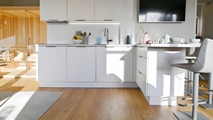 A modern kitchen with white cabinetry, a large island, a built-in oven, and a flat-screen TV. - Helle Deel – Bright Holiday Apartment with Sauna and Terrace (Fehmarn)