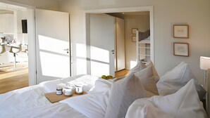 A hotel room with a bed, a bedside table with a cup and a book, a door leading to a bathroom, and a wall with framed pictures. - Helle Deel – Bright Holiday Apartment with Sauna and Terrace (Fehmarn)