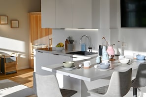 A modern kitchen with white cabinetry, a central island with seating, and a dining area with chairs and bowls.