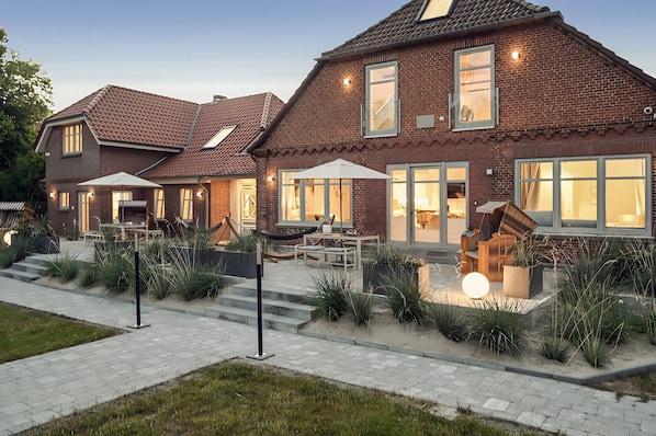 A two-story brick house with a patio, outdoor seating, and a well-lit entrance.