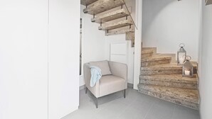 A staircase with wooden steps and a light fixture, a beige armchair with a blanket, and a white door. - Lütter Lünk – Exclusive Loft with Terrace (Fehmarn)