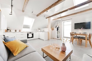 A modern living space with a kitchen, dining area, and a loft bedroom with a skylight.