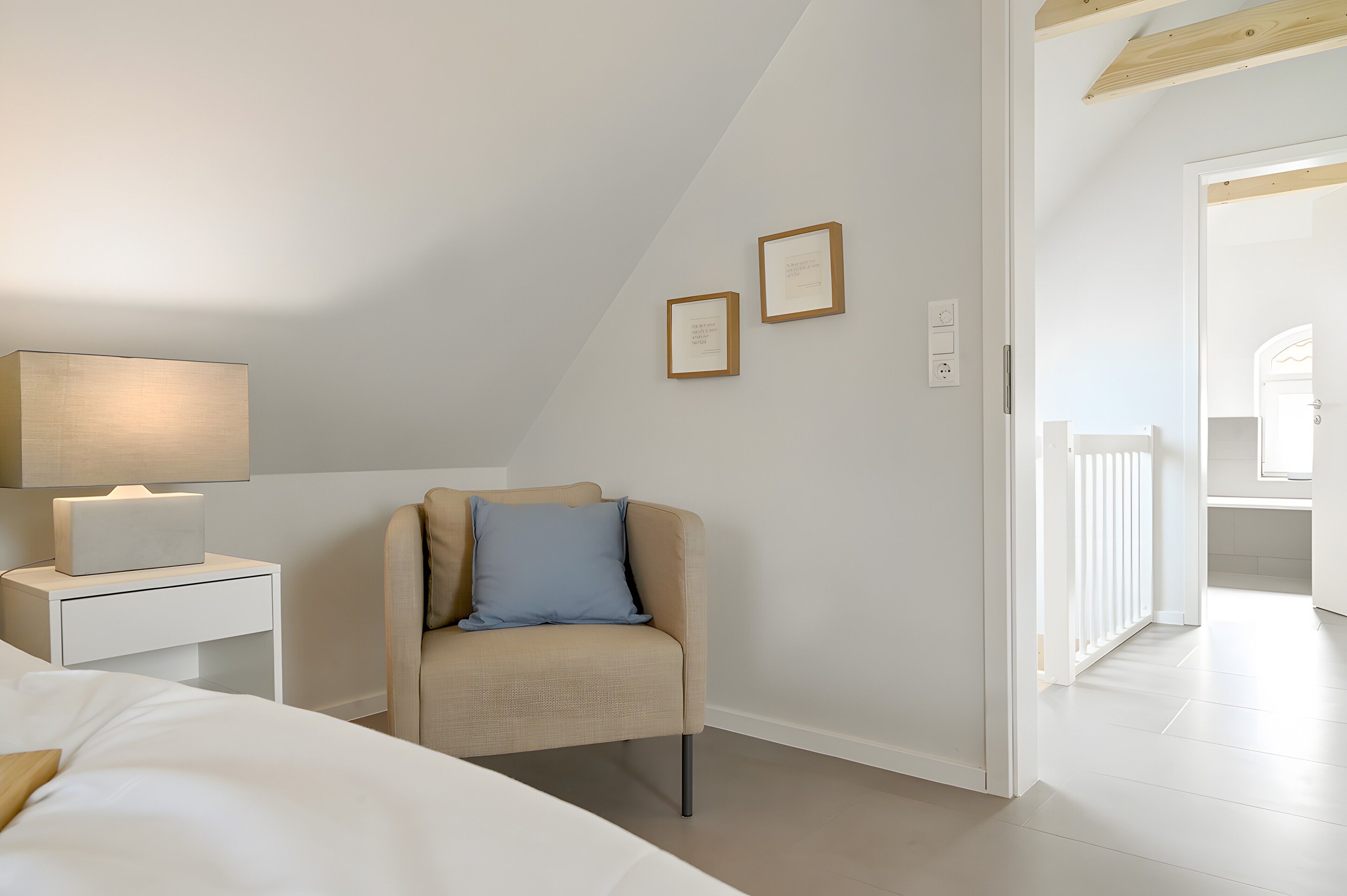 A bedroom with a bed, a nightstand with a lamp, a chair, and two framed pictures on the wall.