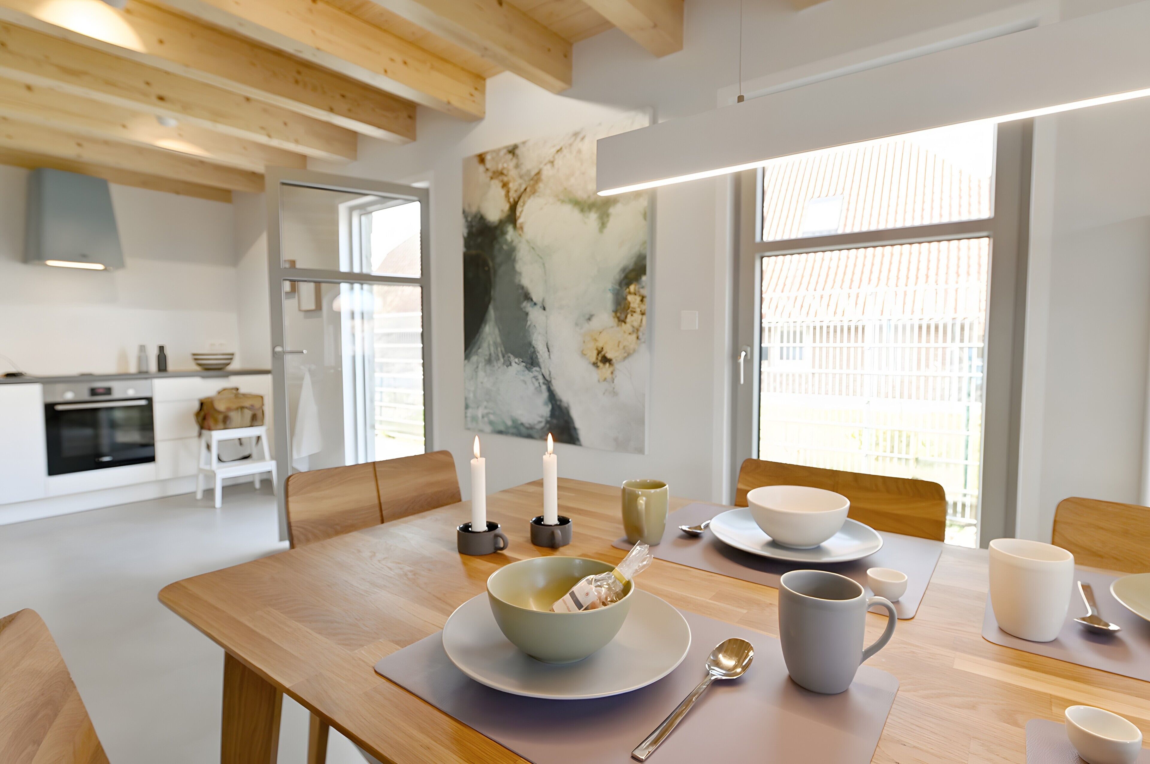 A modern kitchen with wooden beams, a dining table set with bowls, cups, and a candle.
