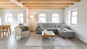 A modern living room with a sofa, armchair, coffee table, and a dining area with chairs and a table.