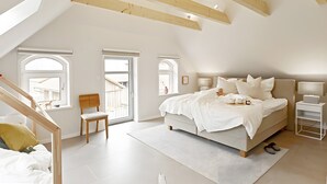 A bedroom with a sloped ceiling, a bed, a chair, a desk, and a window.