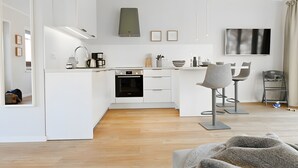 Una cocina moderna con armarios blancos, horno empotrado y una zona de comedor con televisor y taburetes de bar.