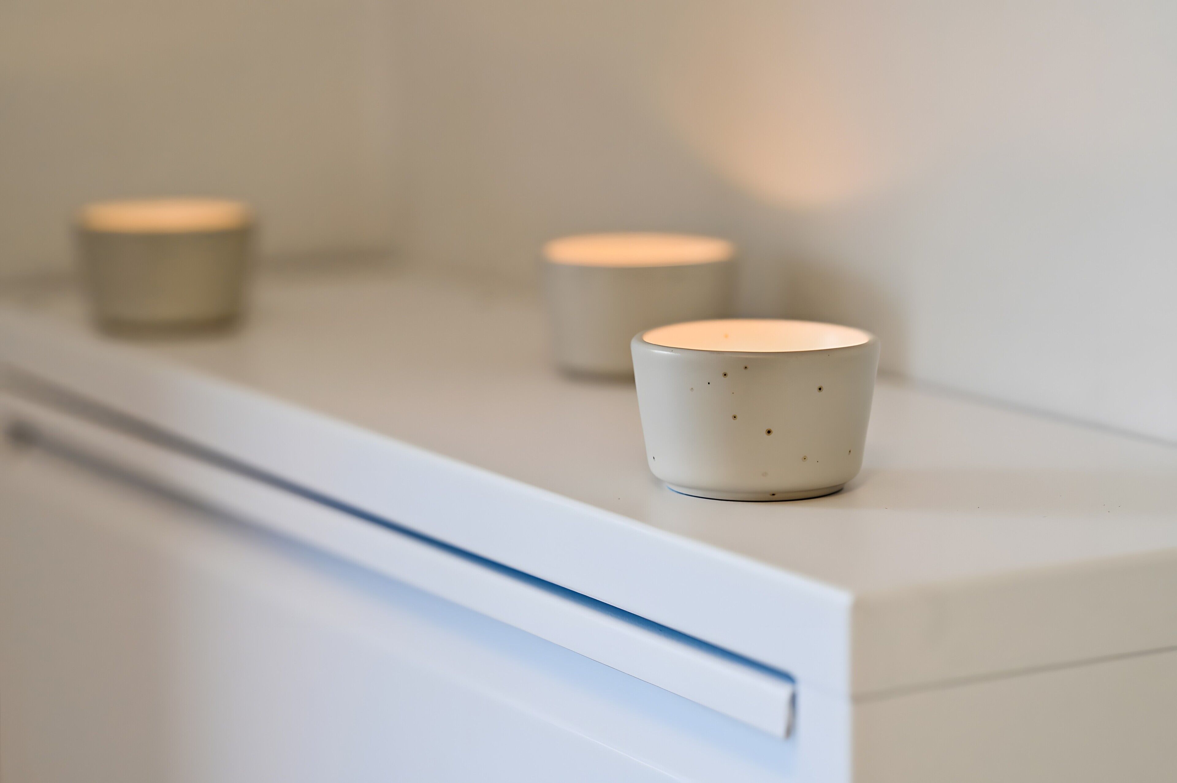 Drie witte keramische bekers op een witte plank.