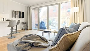Una sala de estar moderna con sofá, una mesa de centro, televisor y un amplio ventanal corredero que da a un área exterior.