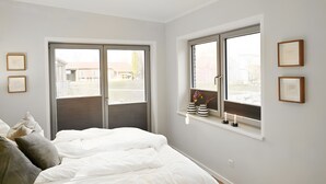 Un dormitorio con una cama, dos ventanas y una estantería con diplomas enmarcados.