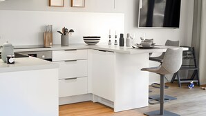 Una cocina moderna con armarios blancos, una isla integrada, un televisor de pantalla plana y un comedor con mesa y sillas.