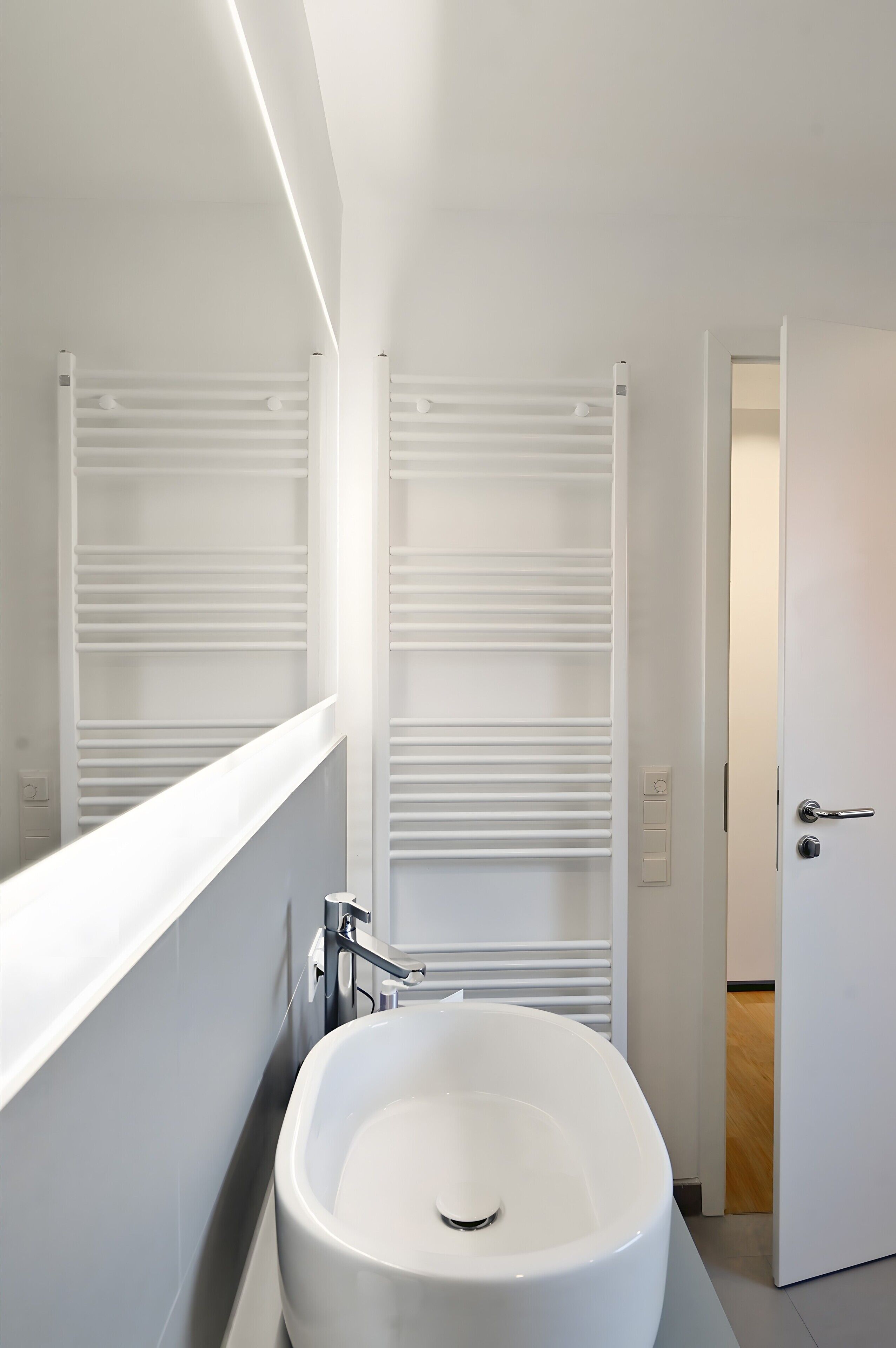 Ein modernes Badezimmer mit einer freistehenden Badewanne, weißen Handtuchhaltern und einer Tür zu einem weiteren Raum.
