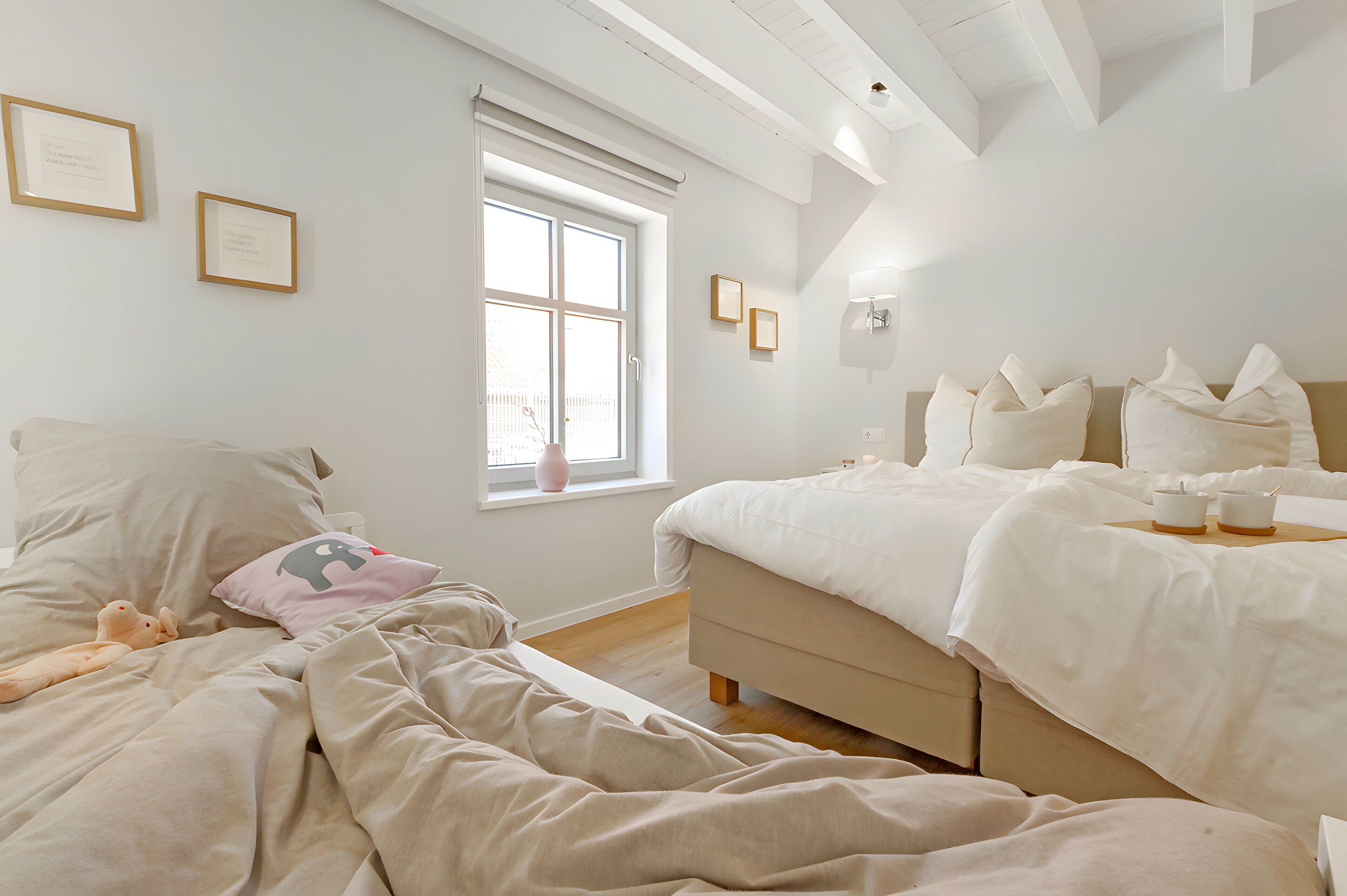 A bedroom with a bed, bedside table, window, and wall-mounted light fixture.