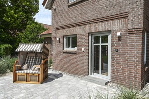A brick house with a sliding glass door, a patio with a wicker chair, and a small outdoor seating area.