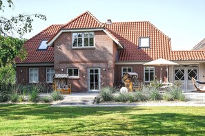 A two-story house with a red-tiled roof, a brick facade, and a front porch with outdoor furniture.