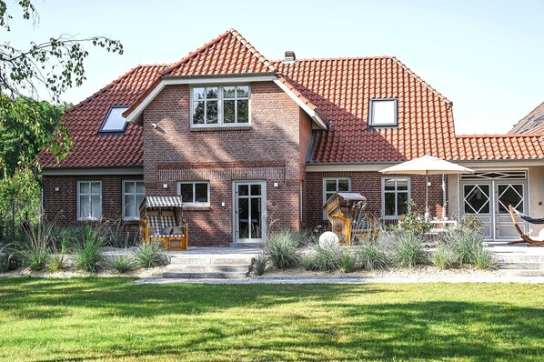 A two-story house with a red-tiled roof, a brick facade, and a front porch with outdoor furniture.