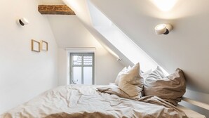 A bedroom with a sloped ceiling, a bed with beige bedding, and two wall-mounted light fixtures. - Mittenmang – Beautiful Holiday Home with Sauna and Terrace (Fehmarn)