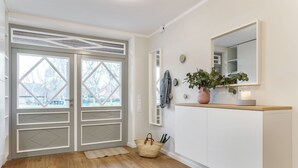 A hallway with a wooden floor, a white cabinet with a mirror, a potted plant, and a woven basket. - Mittenmang – Beautiful Holiday Home with Sauna and Terrace (Fehmarn)