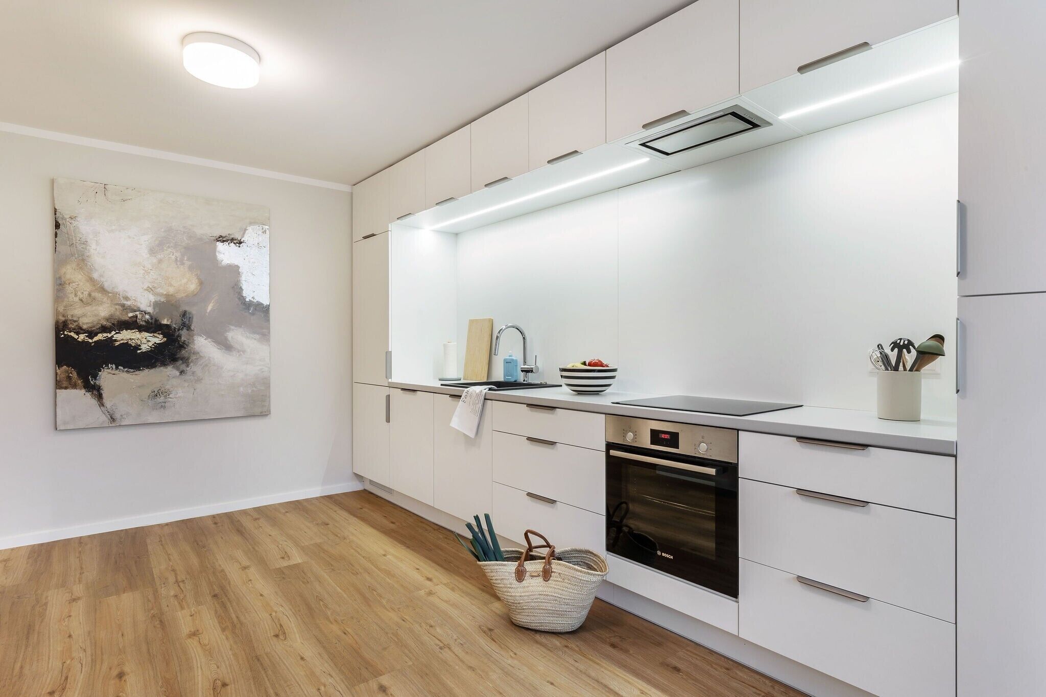 A modern kitchen with white cabinets, a built-in oven, and a large abstract painting on the wall.