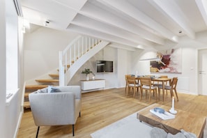 A modern living room with a staircase, a dining area, and a TV mounted on the wall.