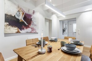 A modern dining area with a wooden table set for four, a large abstract painting on the wall, and a minimalist design.