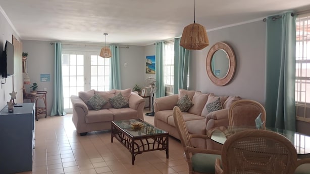 A living room with two sofas, a coffee table, wicker chairs, a TV, and a large mirror.