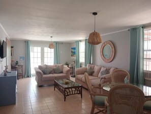 A living room with two sofas, a coffee table, wicker chairs, a TV, and a large mirror. - Charming 2-bedroom bungalow in fabulous Willemstad with AC (Willemstad)