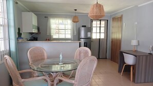 A modern kitchen with a round glass table surrounded by wicker chairs, a refrigerator, and a wooden cabinet.