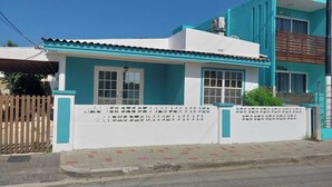 A two-story building with a white and blue facade, a gated entrance, and a visible balcony on the upper floor.