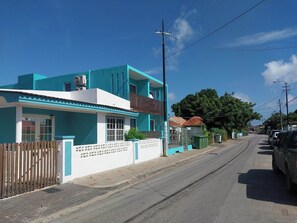 A two-story building with a blue and white facade, a wooden fence, and a paved street with parked cars. - Charming 2-bedroom bungalow in fabulous Willemstad with AC (Willemstad)