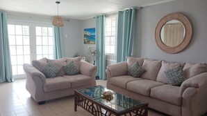 A living room with two beige sofas, a glass coffee table, and a round mirror on the wall.