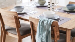 Un tavolo da pranzo con sedie in legno, una ciotola, piatti e bicchieri.