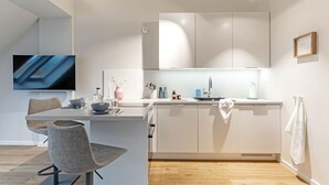 A modern kitchen with white cabinets, a built-in oven, a sink, and a flat-screen TV mounted on the wall. - Achterdörn Een – Beautiful Loft for Relaxation (Fehmarn)