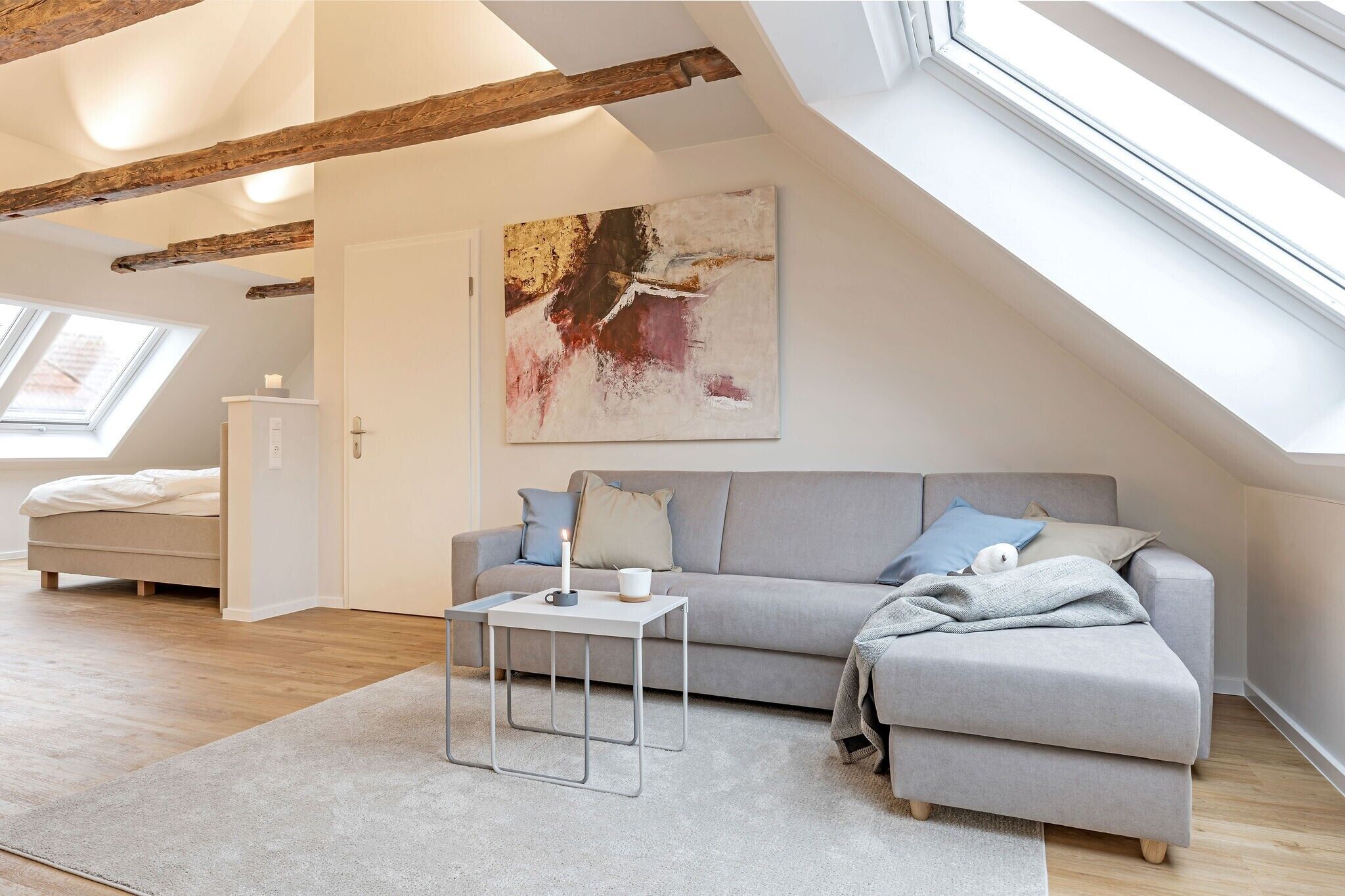 Ein modernes Schlafzimmer im Loft-Stil mit schrägen Wänden, einem grauen Sofa, einem kleinen Tisch und einem großen abstrakten Gemälde.