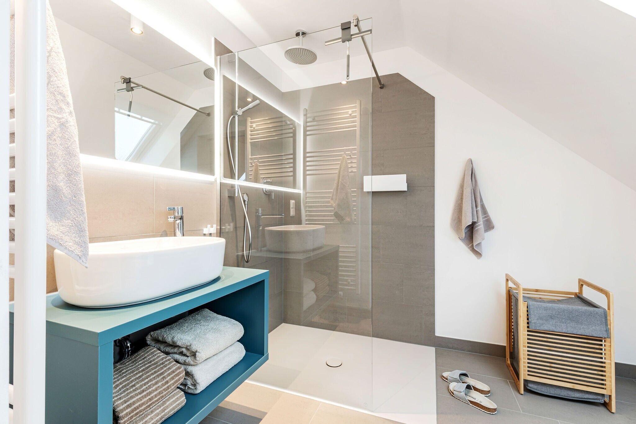 Een moderne badkamer met een glazen douchecabine, een wit wastafeltje en een blauwe badkamerkast.