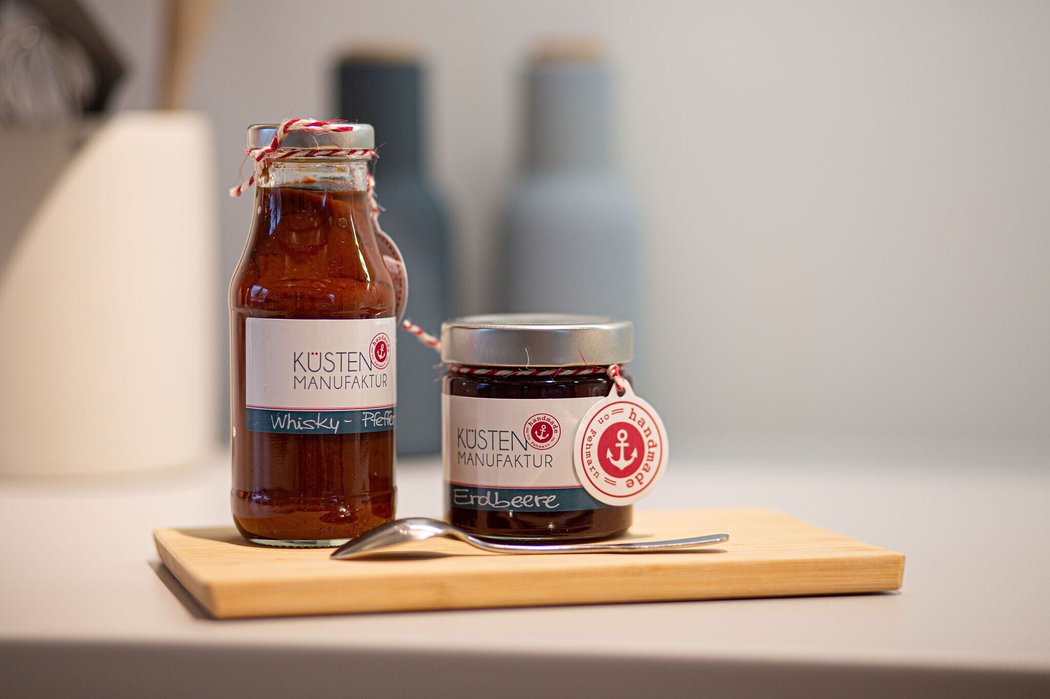 Two bottles of KÜSTEN MANUFÄKTUR whisky on a wooden board with a spoon.