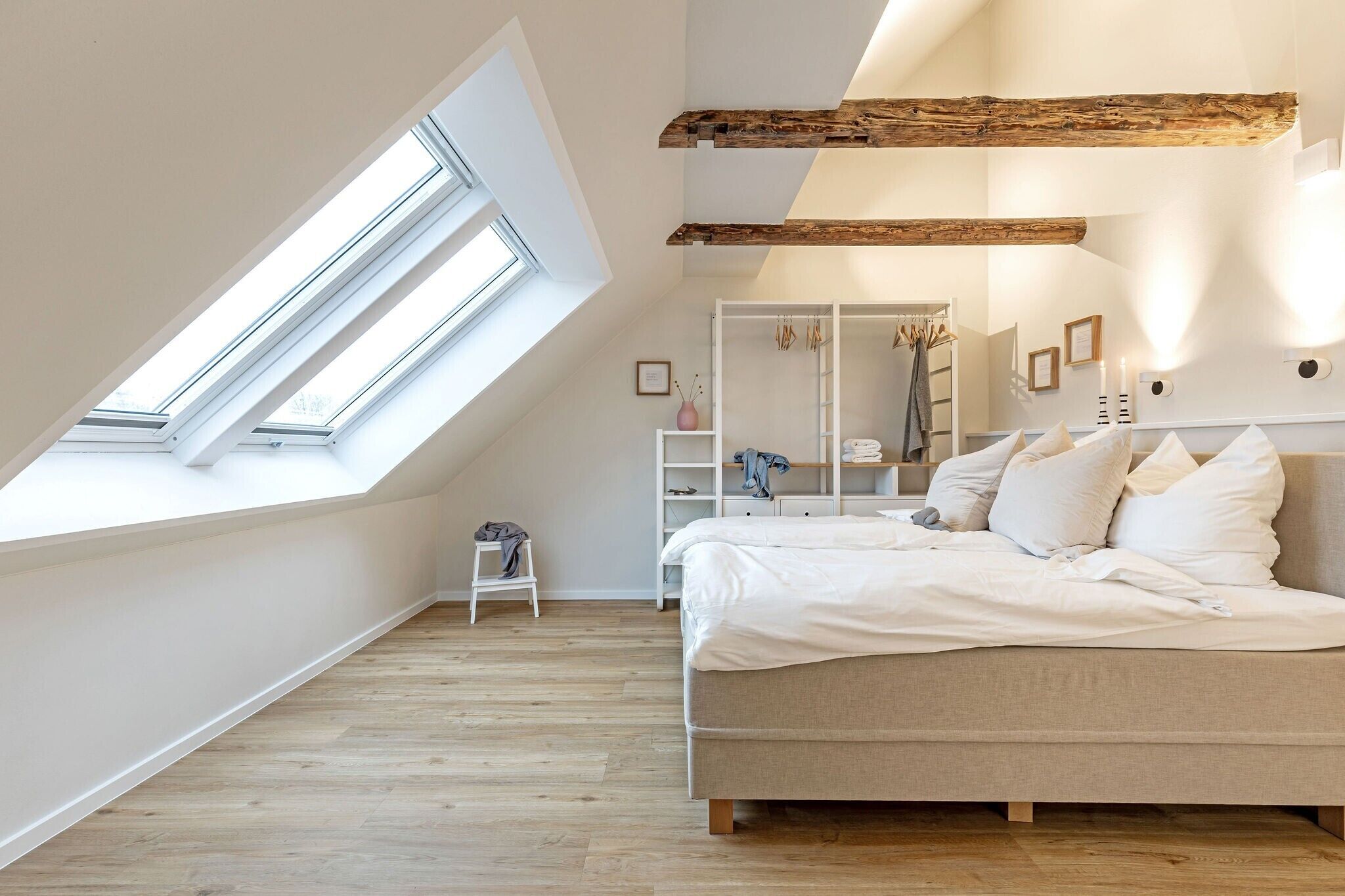 Quarto com teto inclinado, claraboias, cama, guarda-roupa e um pequeno banquinho.